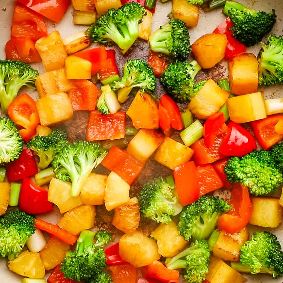 closeup of vegetables and pineapple chunks in a pan being cooked