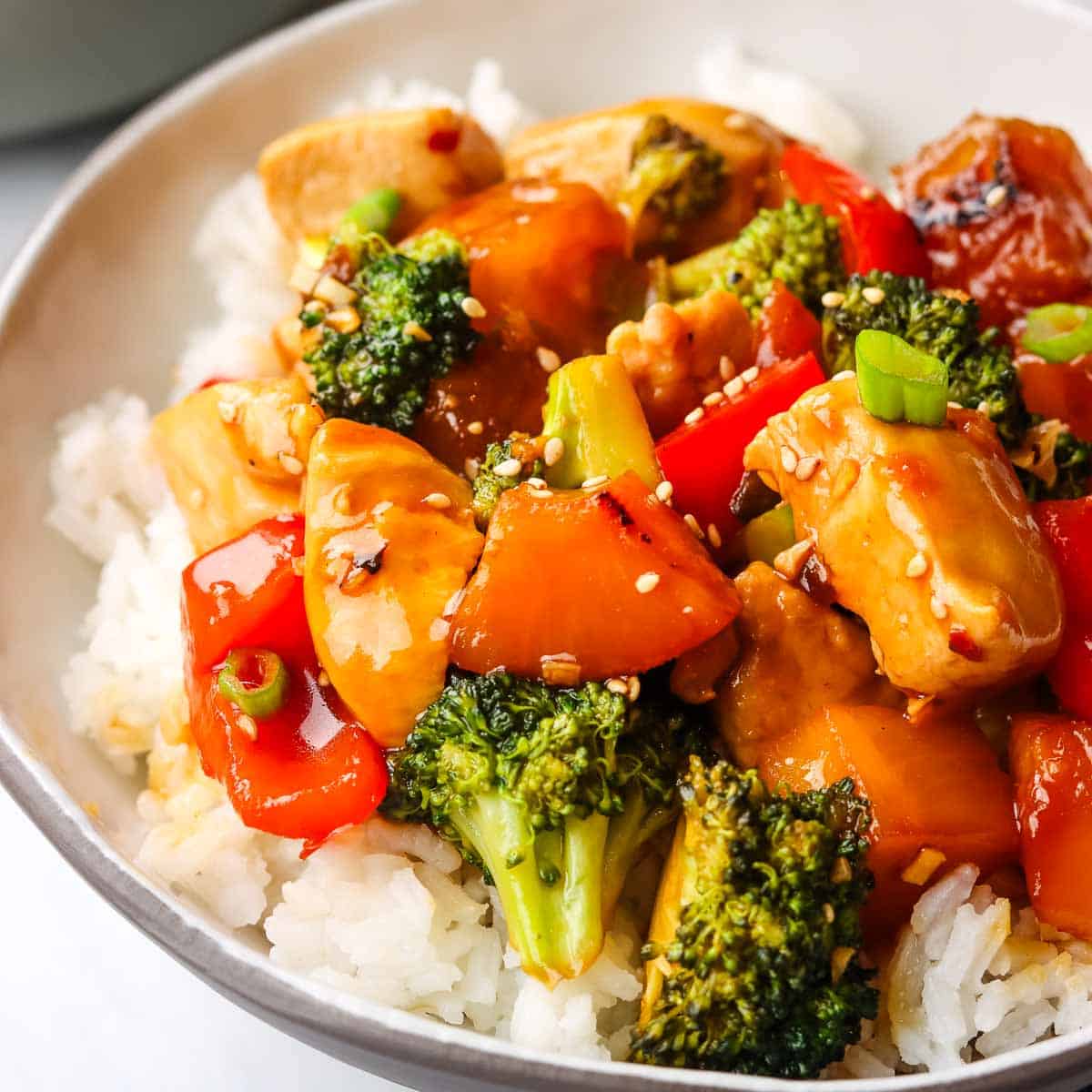 Closeup of a chicken and vegetable teriyaki stir fry on a bed of white rice in a bowl.