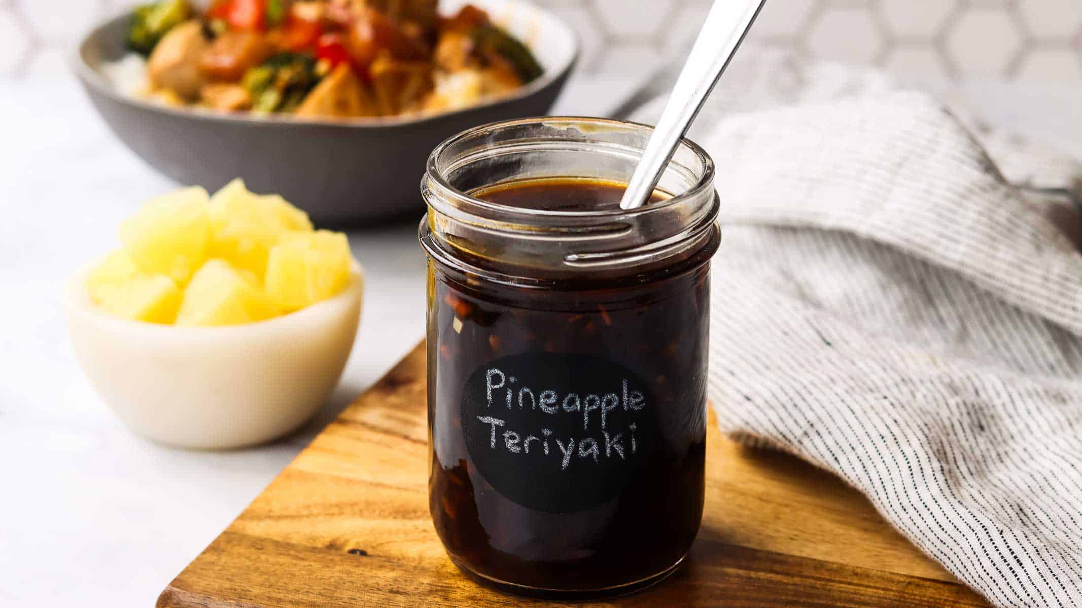 a jar of pineapple teriyaki sauce placed on a cutting board with a spoon in it