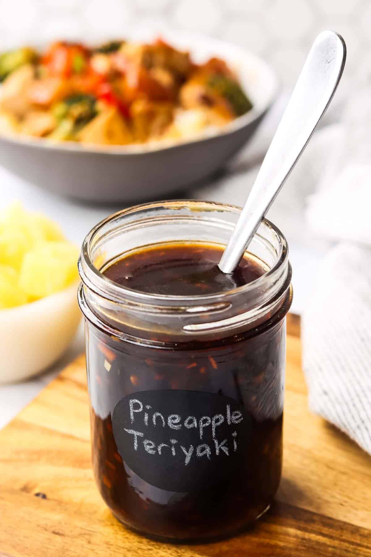 a jar of pineapple teriyaki sauce placed on a cutting board with a spoon in it