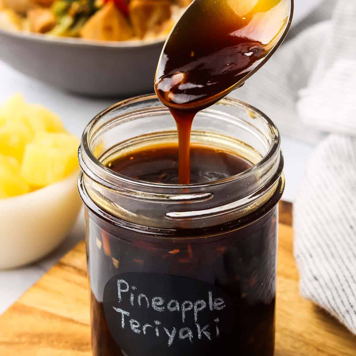 A jar of teriyaki sauce with a spoon drizzling some sauce into the jar to show the consistency.