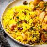 A bowl of yellow rice with raisins and cashews in a bowl with a wooden spoon showing a spoonful.
