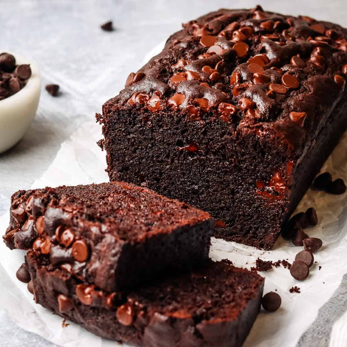 A loaf of chocolate cake with two thick slices stacked in front of it.