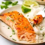A salmon fillet on a plate with a side of white rice and lime wedges, with a bite taken out to show the inside.
