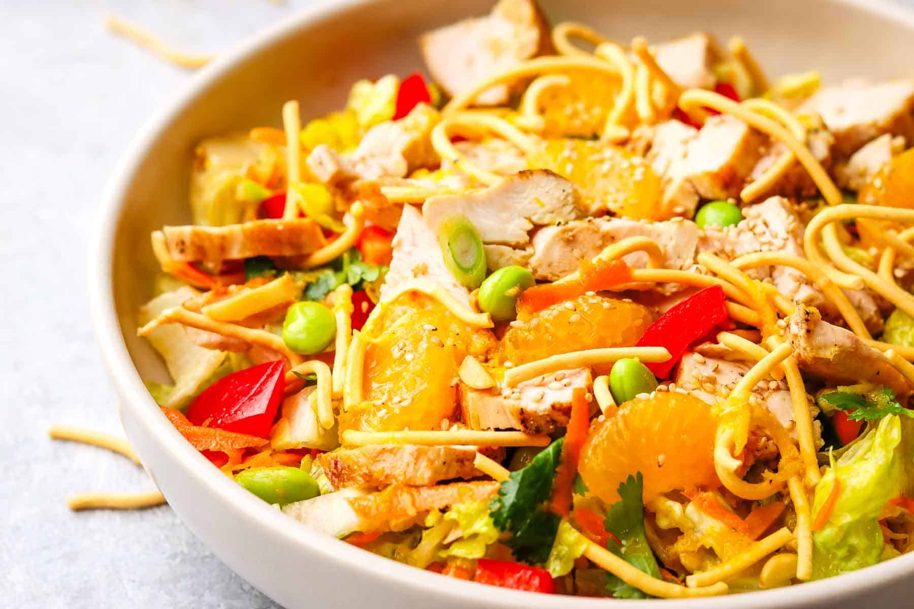A bowl of Asian-inspired salad with chicken and mandarin oranges garnished with chow mein noodles.