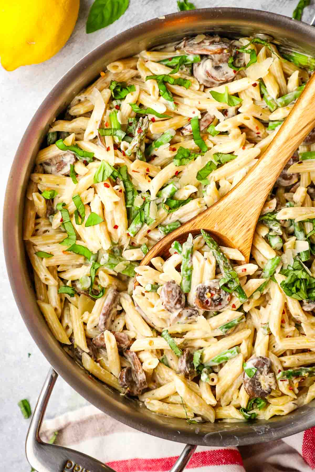 A pan of asparagus mushroom pasta with a wooden serving spoon in it.