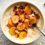 A bowl of oatmeal with caramelized bananas and pecans on top, with a spoon in it.