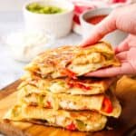 A stack of chicken vegetable quesadillas with a hand picking one up.
