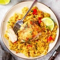 A plate of yellow rice and chicken thighs with a forkful of chicken.