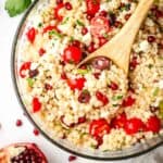 A large serving bowl of Israeli couscous salad with a wooden serving spoon in it.