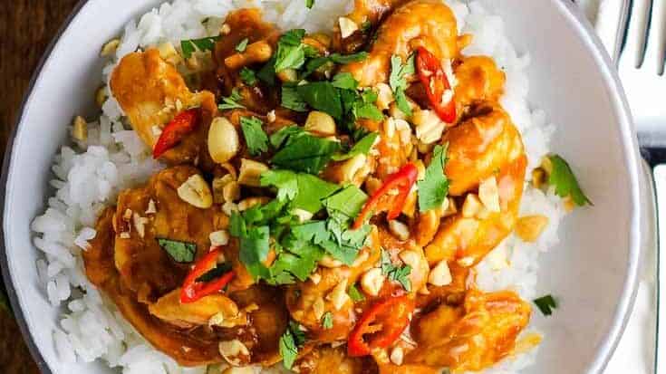 Chicken satay over rice in a bowl garnished with peanuts, cilantro and Thai chiles