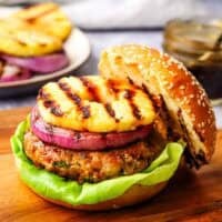 A grilled chicken burger topped with red onion and pineapple.