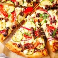 Up close view of a slice of Mediterranean pizza topped with vegetables and cheese.