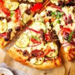 Up close view of a slice of Mediterranean pizza topped with vegetables and cheese.