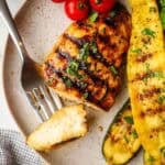 A grilled chicken breast on a plate with a bite on a fork.
