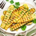 Grilled zucchini and yellow squash on a platter garnished with parsley.