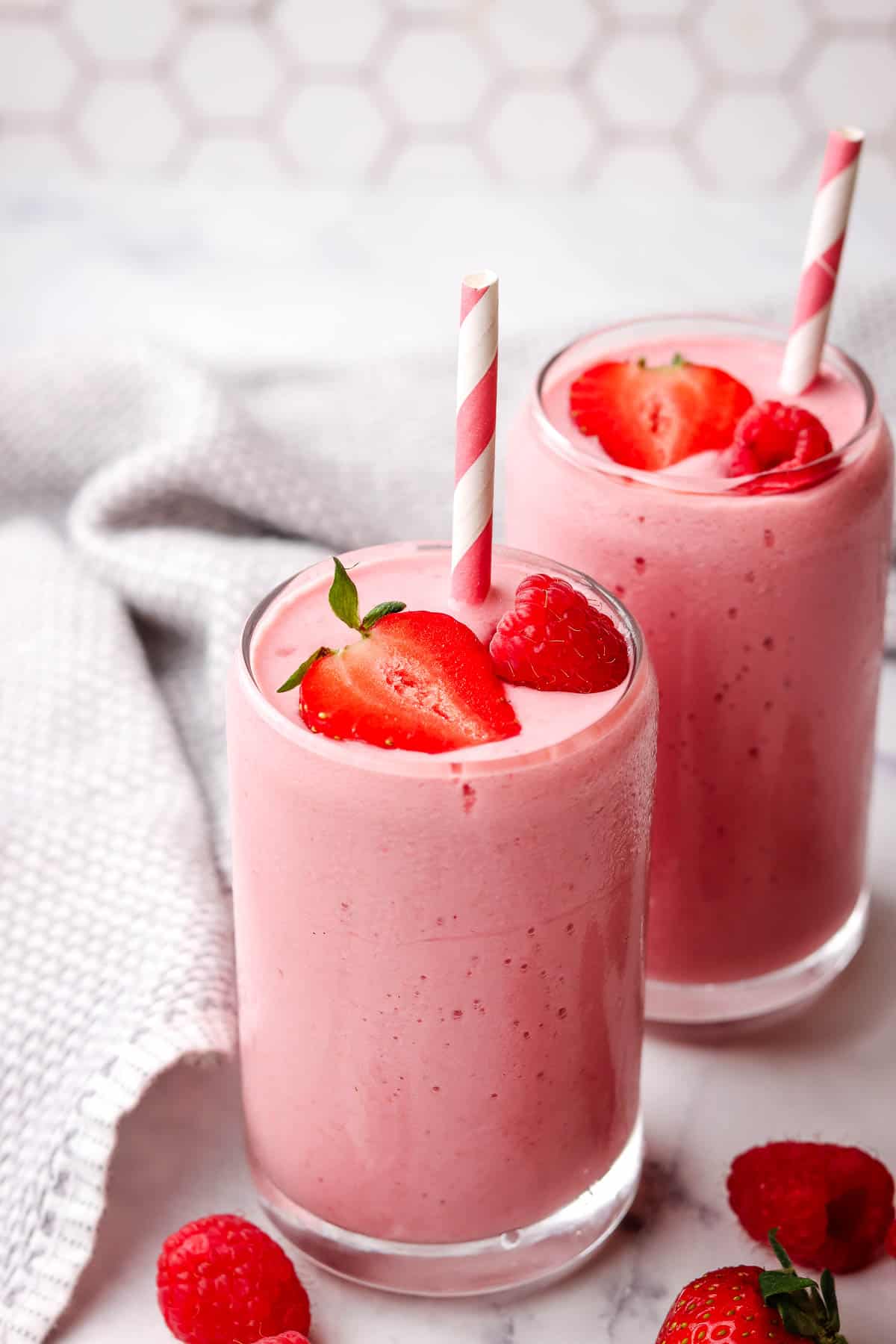 Two pink strawberry raspberry smoothies garnished with berries and a paper straw.