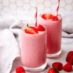 Two pink strawberry raspberry smoothies garnished with berries and a paper straw.