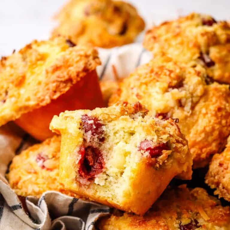 A basket of cherry muffins with one bitten into to show the inside.