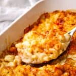 A baking dish of macaroni and cheese with a serving spoon showing a spoonful.