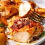 A sliced roasted chicken thigh with sun dried tomato pesto and potatoes on a plate.