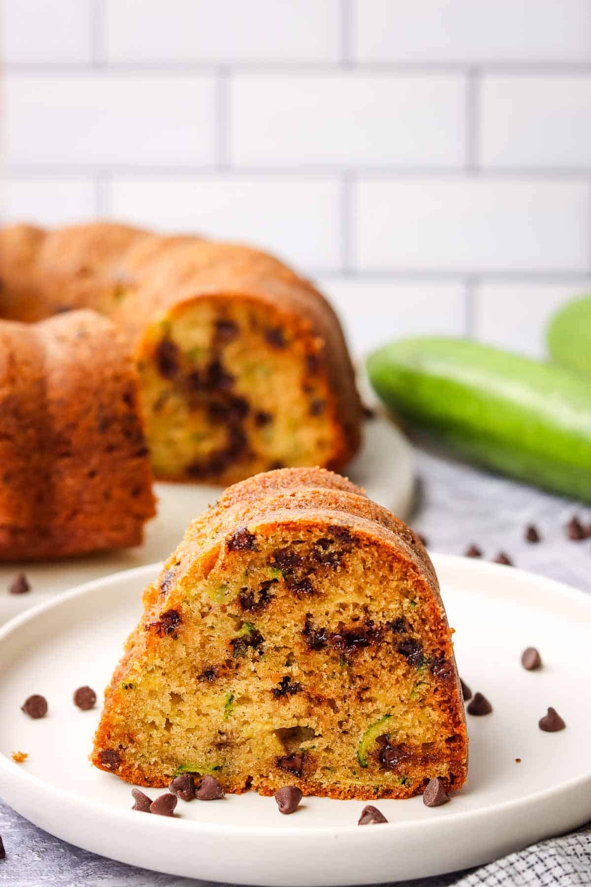 a slice of zucchini bundt cake served on a plate with the whole cake in the background
