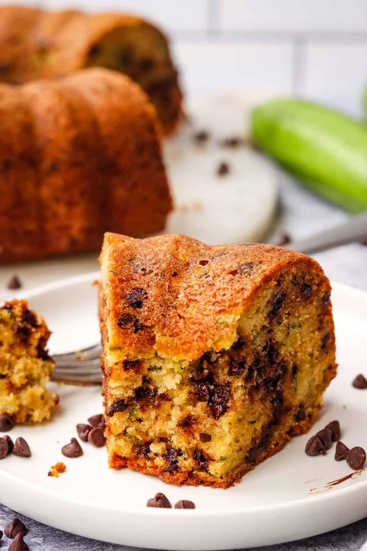 A piece of zucchini bundt cake with chocolate chips with a bite taken out on a white plate.