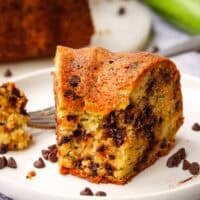 A piece of zucchini bundt cake with chocolate chips with a bite taken out on a white plate.