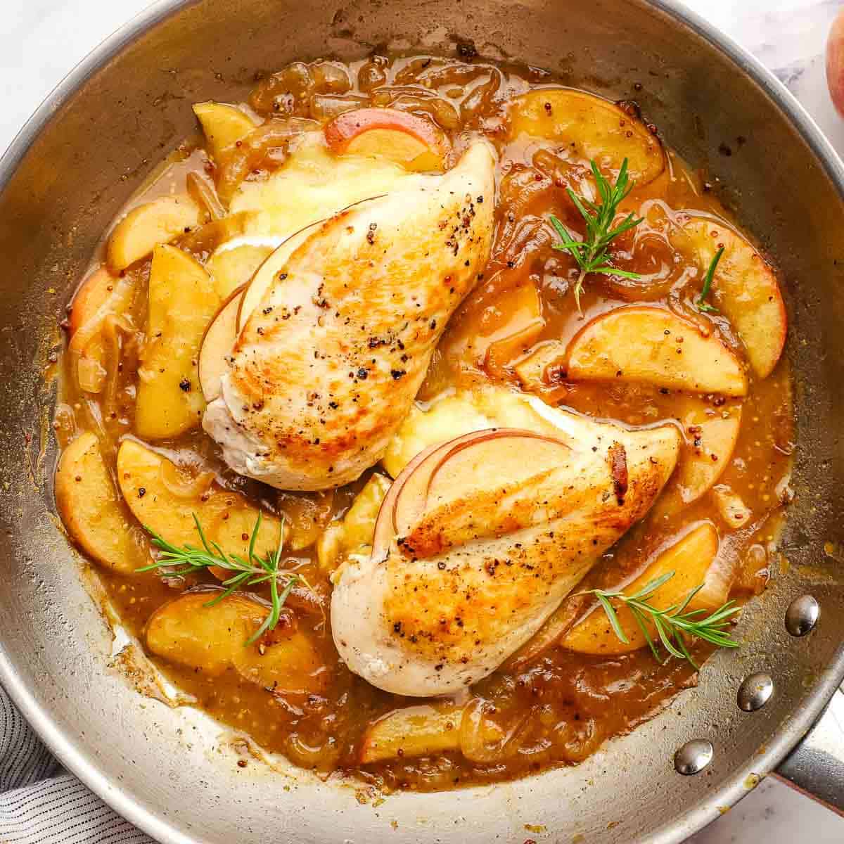 A pan of apple brie stuffed chicken in sauce garnished with rosemary.
