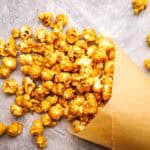 Homemade caramel corn spilling out of a parchment cone.