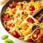 A pan of cherry tomato pasta with tongs.