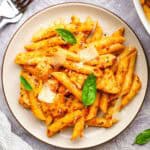 A plate of sun dried tomato pesto chicken pasta garnished with basil leaves and Parmesan.