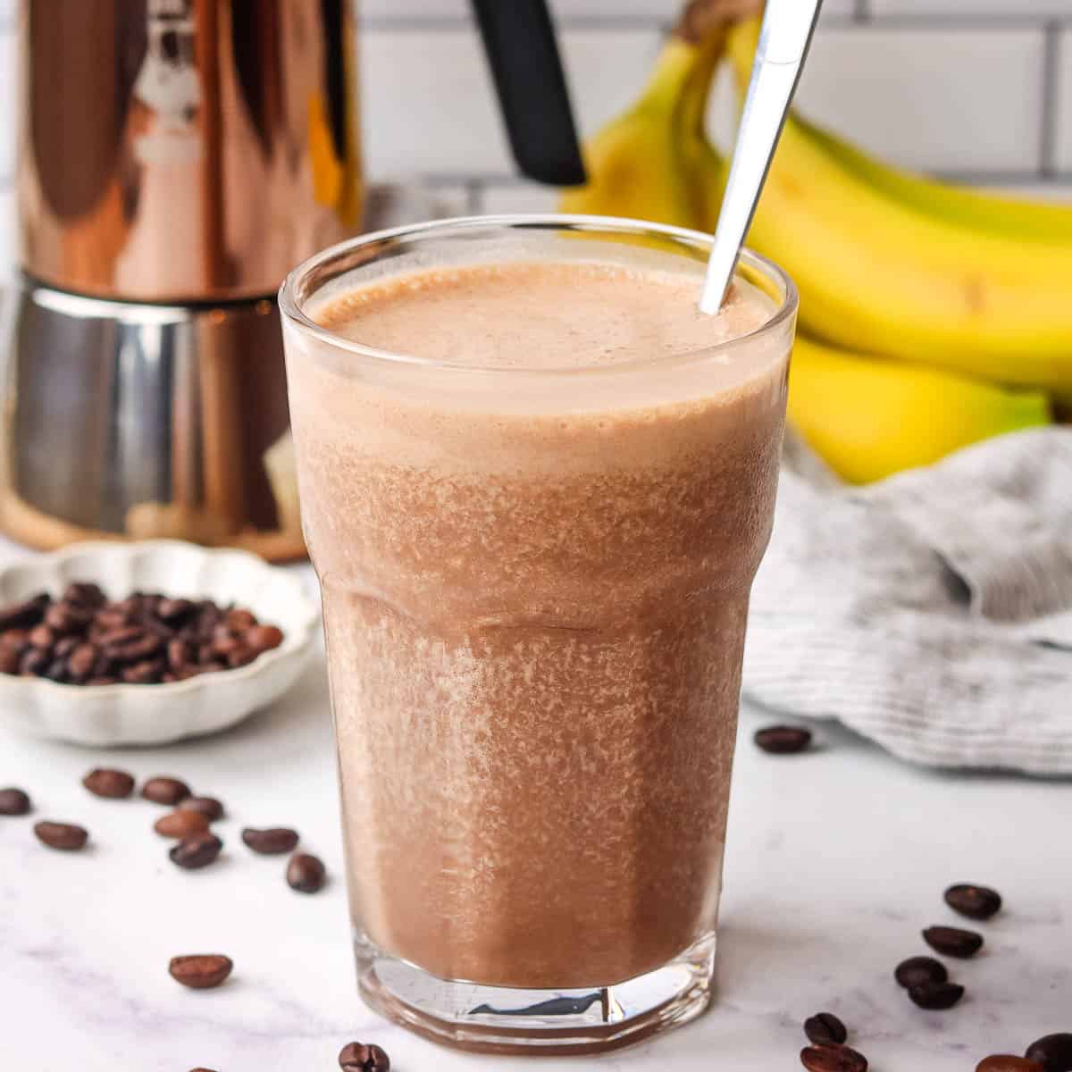 A tall glass of coffee banana smoothie with a spoon in it.