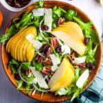 A bowl of salad with thinly sliced pears, and pecans over arugula.