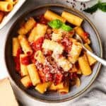 A bowl of rigatoni tossed with roasted tomatoes and garnished with Parmesan and basil.