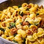 A pan of sausage kale pasta with a serving spoon in it.