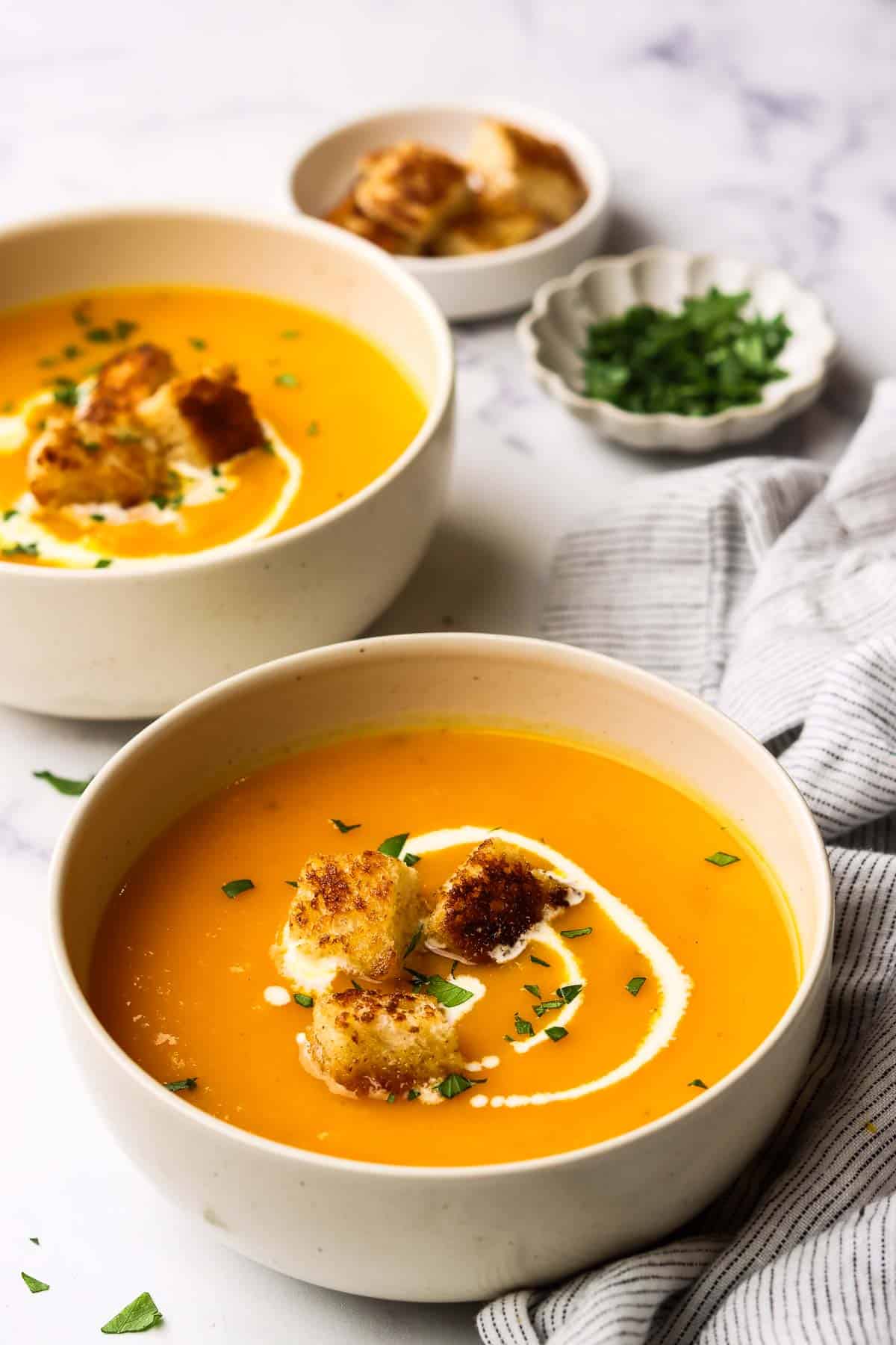 A bowl of butternut squash soup garnished with cream and croutons.