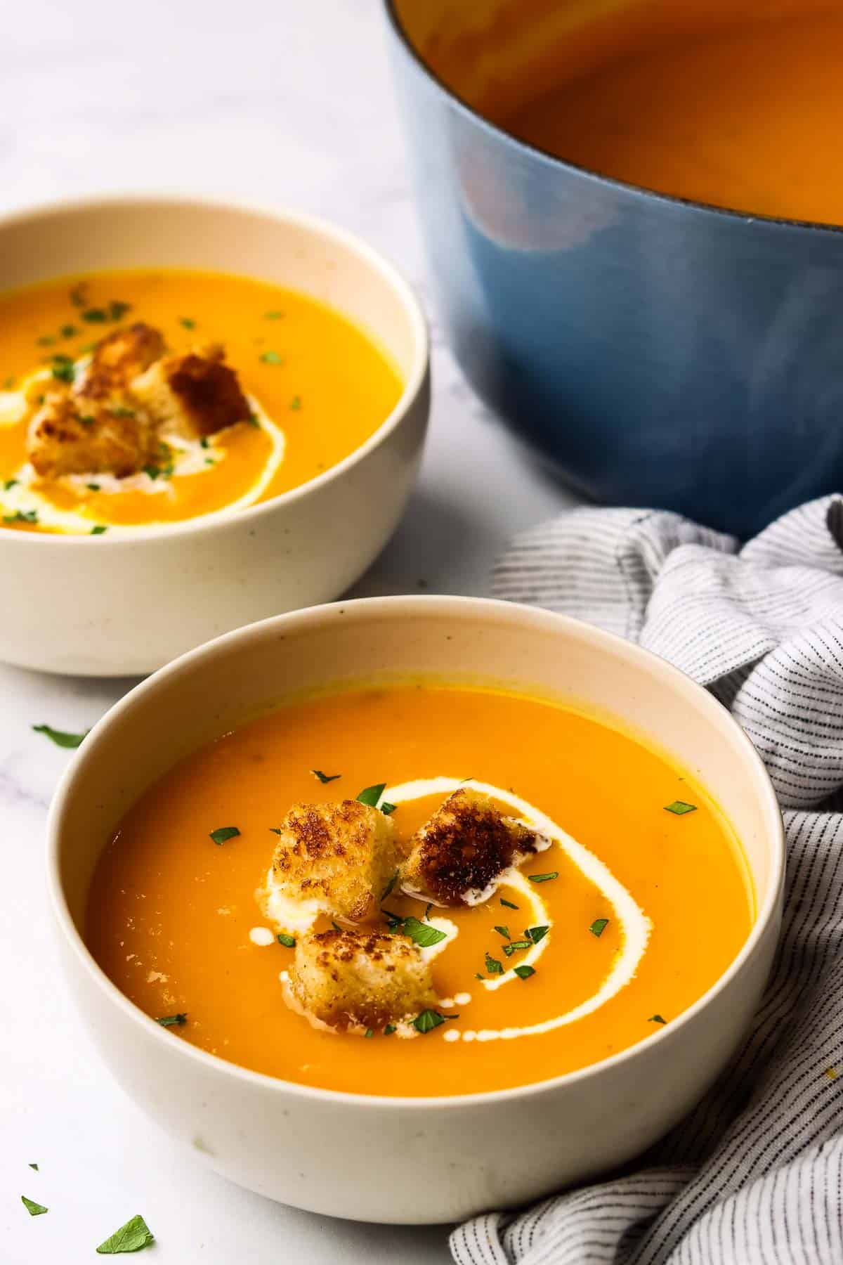 A bowl of butternut squash soup garnished with cream and croutons.