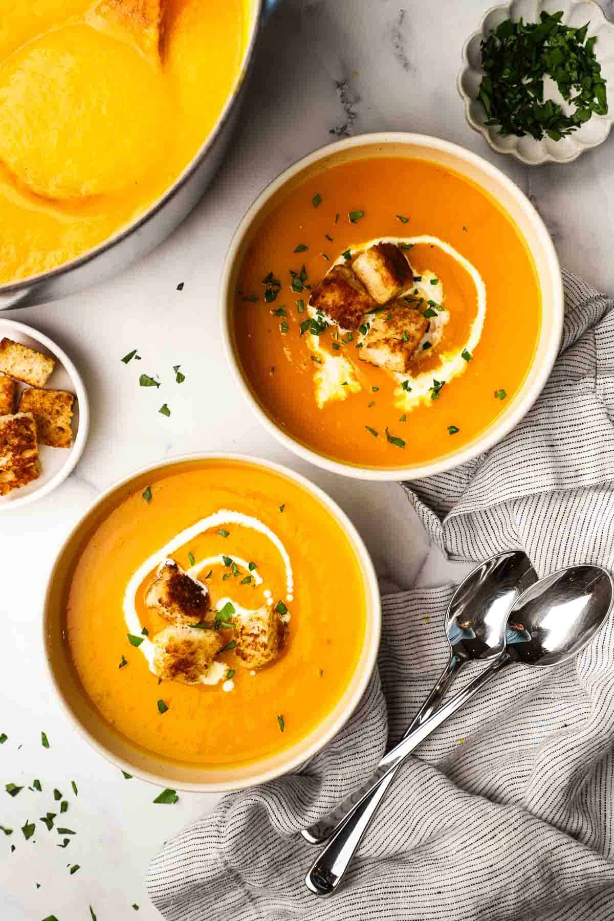 Two bowls of butternut squash soup garnished with cream and croutons.