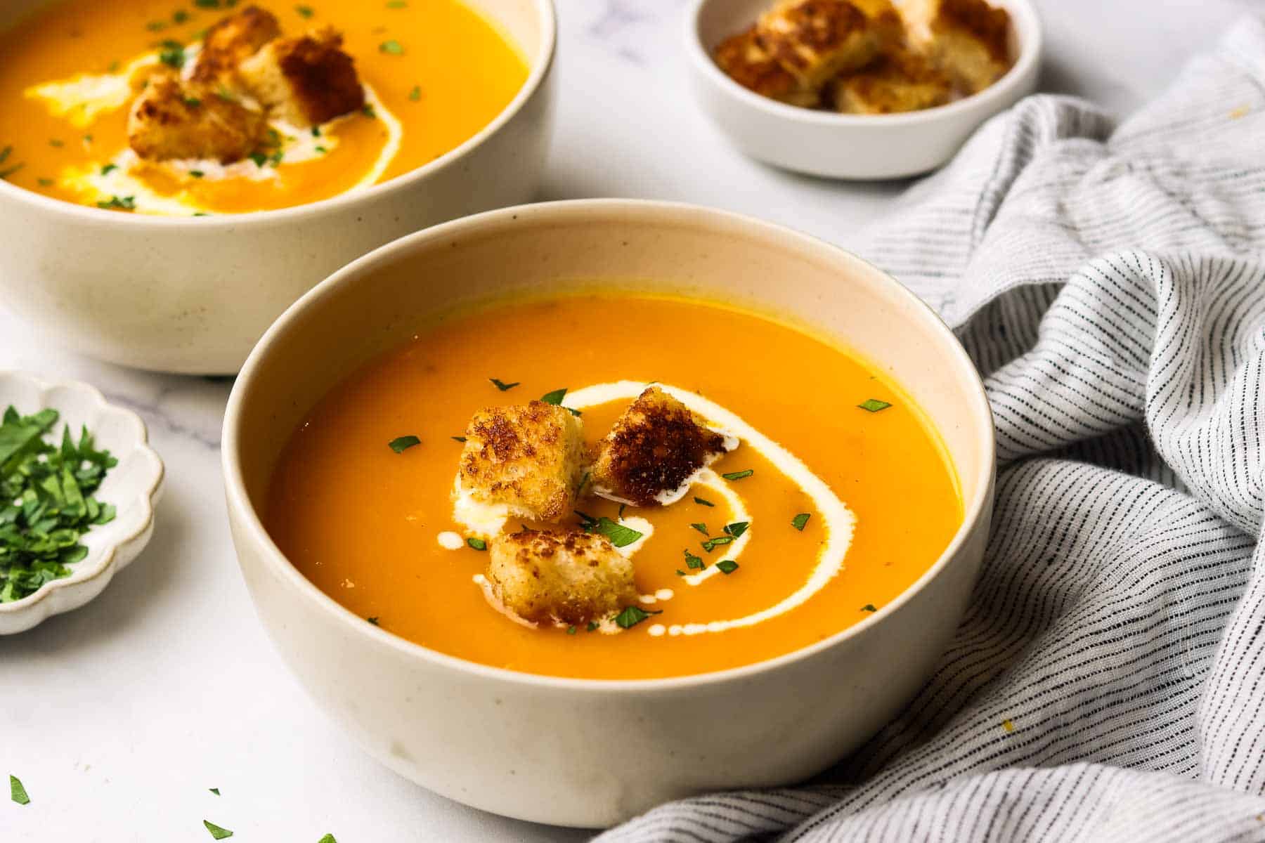 A bowl of butternut squash soup garnished with cream and croutons.