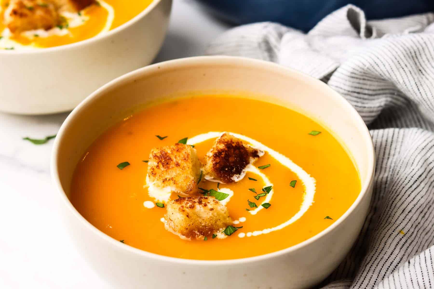 A bowl of butternut squash soup garnished with cream and croutons.