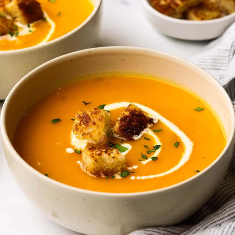 A bowl of butternut squash soup garnished with cream and croutons.