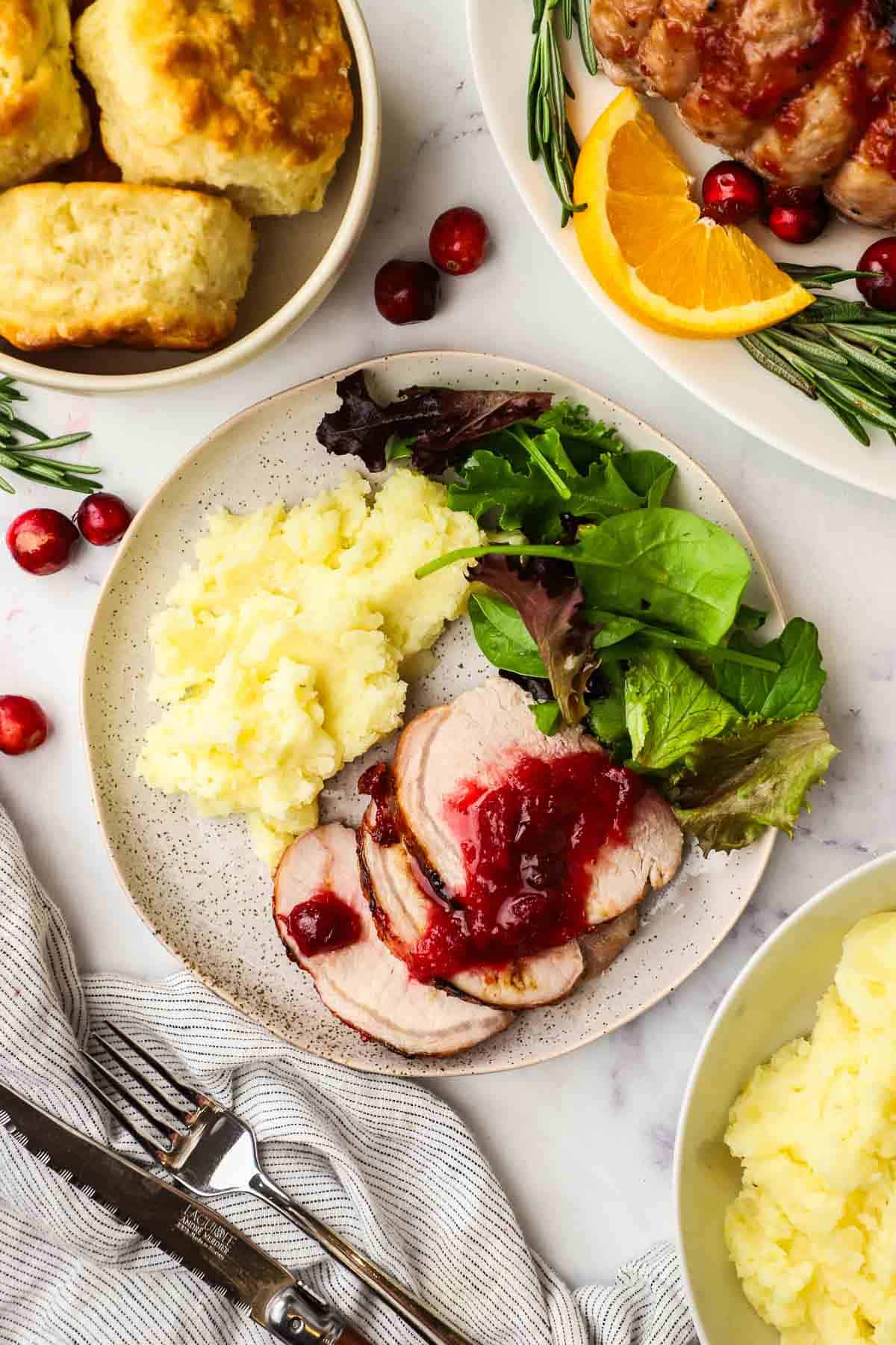 cranberry glazed pork loin roast served on a plate with some mashed potatoes and greens