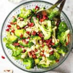 A serving bowl of fresh broccoli salad with serving utensils in it.