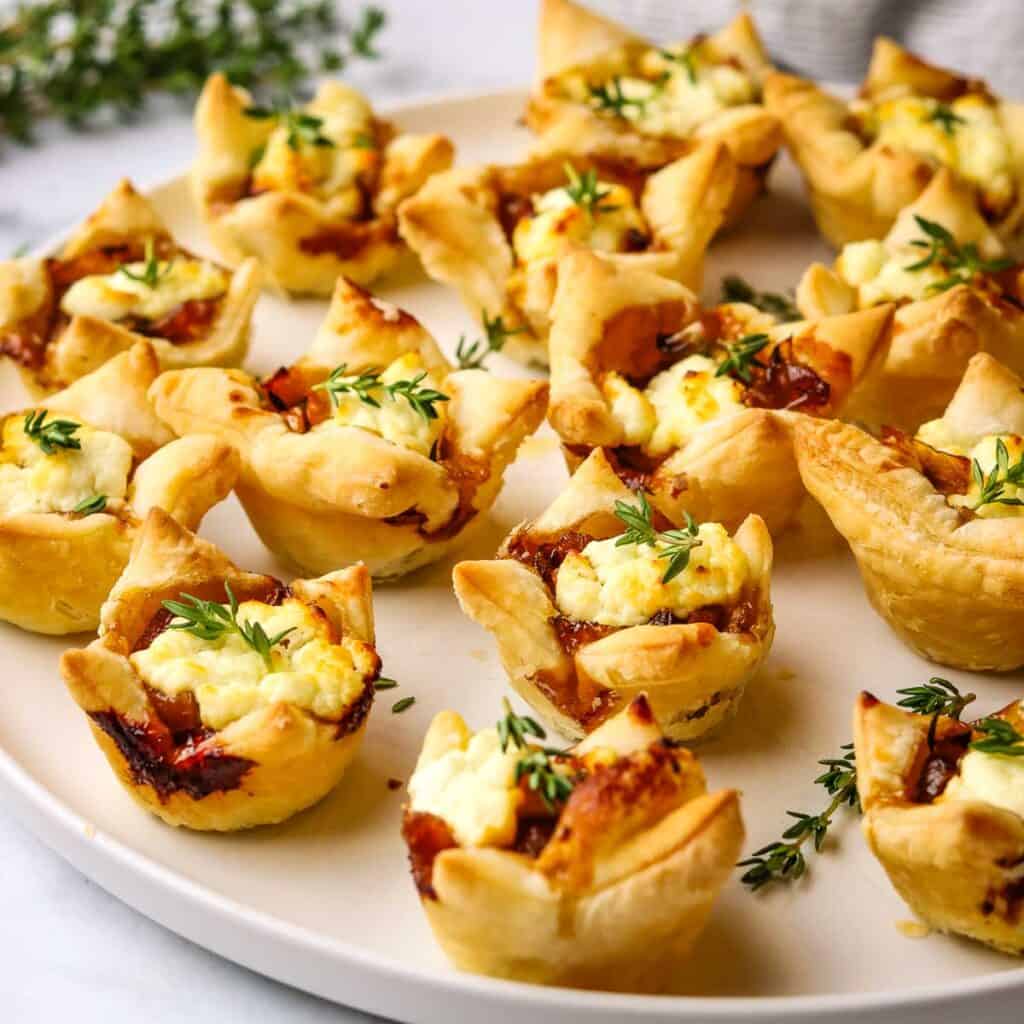A platter of caramelized onion and goat cheese tarts garnished with fresh thyme.
