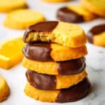 A stack of round shortbread cookies half dipped in chocolate with a bite taken out of the top one.