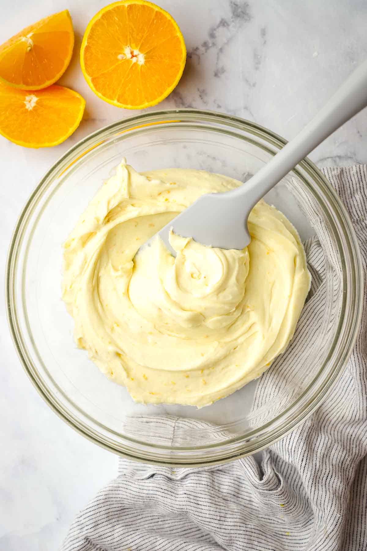 A bowl of orange cream cheese frosting with a silicone spatula in it.