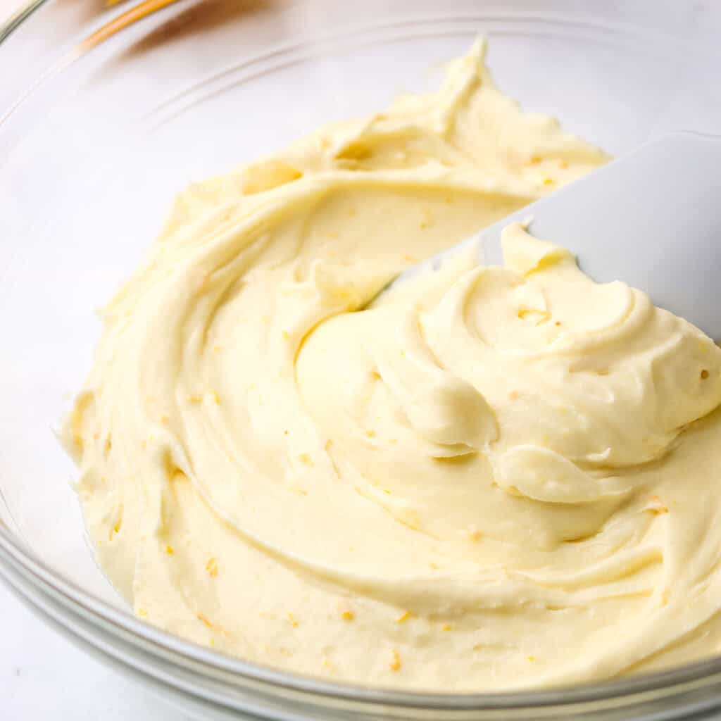 A bowl of orange cream cheese frosting with a silicone spatula in it.
