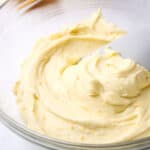 A bowl of orange cream cheese frosting with a silicone spatula in it.