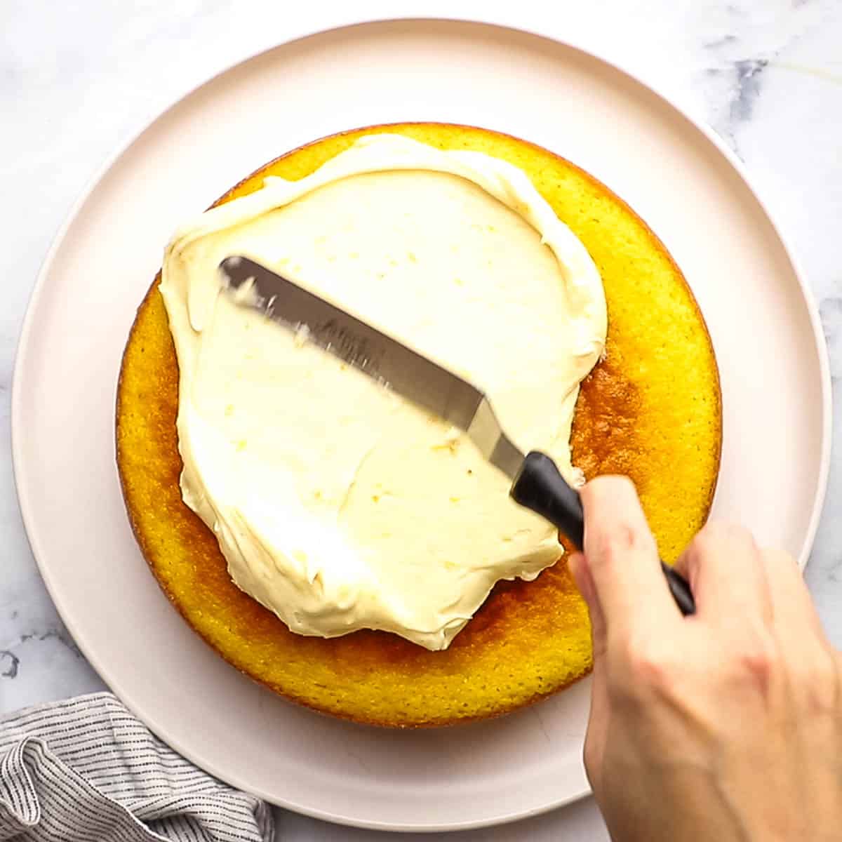 a hand spreading frosting on the middle layer of the cake with an offset spatula
